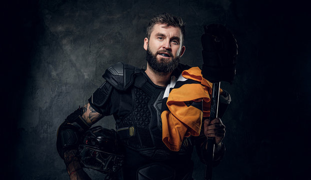 Portrait of serious bearded hockey player with his sport gear in hands.