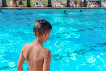 European boy taking off to jump into swimming pool. Back view.