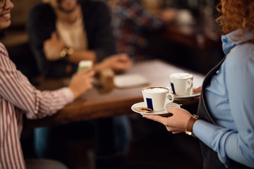Unrecognizable waitress serving guests with a coffee in a cafe.