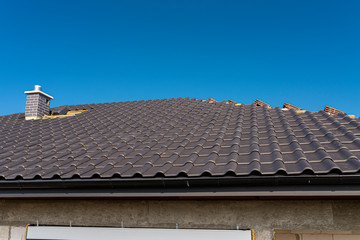 The roof of a single-family house covered with a new ceramic tile in anthracite, against the blue sky.