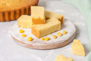 Freshly baked corn bread on a round wooden white board with corn on a light background.