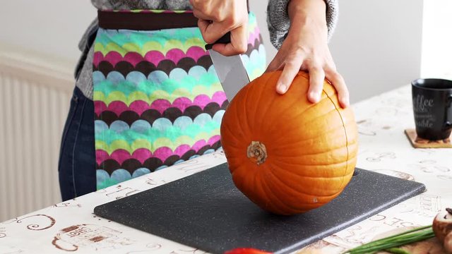 Woman cutting a pumpking on the table with a chef knife to make pumpking soap for the halloween
