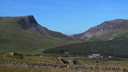 Panning shot from the hill opposite of Rhyd Ddu village showing mountain landscape between lake LLyn y Gadair (only small part seen) and Llyn Cwellyn with Rhyd Ddu in between on a sunny day.