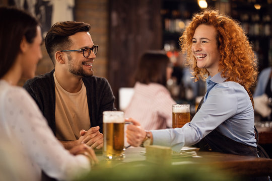Cheerful waitress serving beer to her guests in a bar.