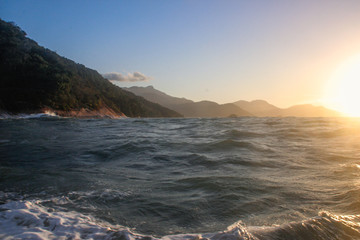 Fototapeta na wymiar Atlantic ocean with rippling water and sea foam and mountains at sunset. Landscape with the beach of Brazil on the island of Ilha Grande.