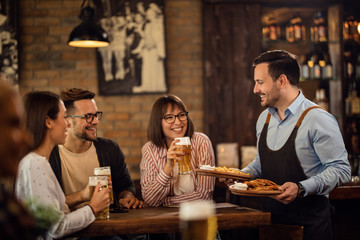 Group of happy friends drinking beer while waiter is serving them food in a pub.