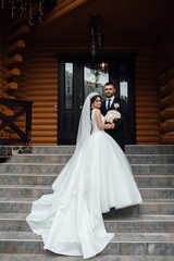 Stylish couple of happy newlyweds posing walking up the stairs on their wedding day. Perfect couple bride, groom posing and hugging. Wedding dress. Bridal wedding bouquet of flowers