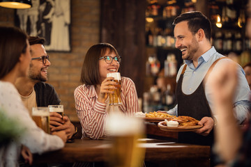 Happy waiter serving group of friends in a pub.