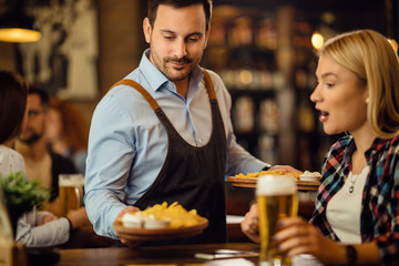 Smiling waiter serving tortilla chips to a woman in a pub.