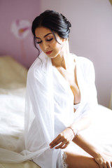 Morning of beautiful bride near the wedding dress. Bride in a white robe  holds and  admires her wedding dress. Beautiful woman with professional make up and hair style. Morning of the bride. 