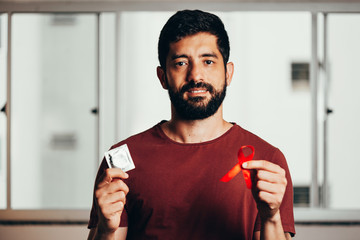 Man holding condom and red ribbon for HIV illness awareness, 1 December World AIDS Day concept.