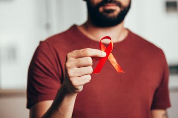 Man holding red ribbon for HIV illness awareness, 1 December World AIDS Day concept. - obrazy, fototapety, plakaty