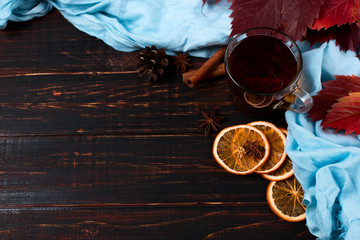 Red autumn leaves, scarf, tea, cinnamon and dried oranges on a wooden table formed a frame, copy space.
