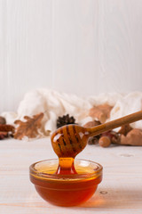 Honey, stick, jar, scarf, dry leaves. Rustic sweet autumn photo, white wooden background, copy space.