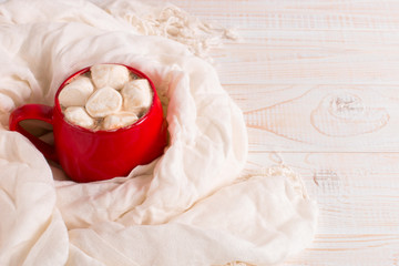 Red mug with cocoa and marshmallows on a white table scarf background. Autumn mood, a warming drink. Copy space.