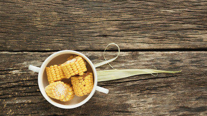 Corn in a bowl with pens. The ear is cut into four pieces. White dishes stand on a table of old wooden boards. Top view, horizontal orientation