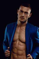 Elegant, muscular, young handsome man posing in fashionable suit on a naked torso, isolated on black background.