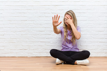 young blonde pretty woman covering face with hand and putting other hand up front to stop camera,...