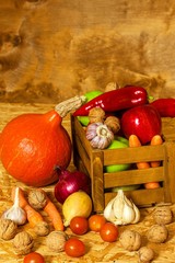 Apples and vegetables in a wooden box on the table. Autumn harvest of fruits and vegetables. Apples, peppers, garlic, nuts and tomatoes on wooden board. Healthy food.