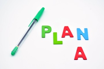 La palabra plan, hecha con letras de madera, acompañada de un boli verde