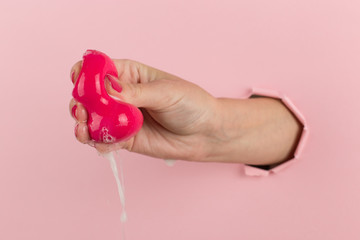 Girl hand holds a beauty blender for makeup from a hole in a pink background, copy space. Sponge in soapy foam, how to clean.
