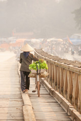 Simple life. Rear view of Vietnamese women with bicycle across the wooden bridge. Vietnamese women with Vietnam hat, vegetable on the bicycle. Rural of north Vietnam. Warm tone.