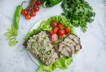 Baked pork chopped in a sauce of walnuts and mint on a white plate with fresh herbs and vegetables. Light background.