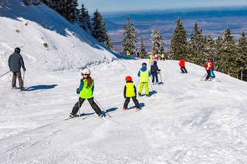 Group of people and kids skiing on a ski slope in Poiana Brasov resort, in winter season, Romania