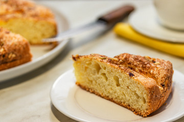 A piece of cake with apples, chopped walnuts and cinnamon lies on a white plate on a light background, close-up