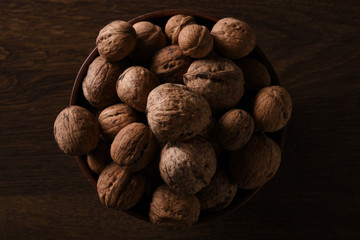   Walnuts nuts in a bowl on a dark brown wooden background in a dark key