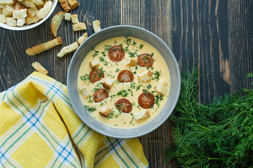 Cheese soup with grilled sausages and herbs. Cream soup served in a plate. Dark wooden background.