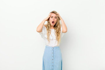 young blonde woman feeling horrified and shocked, raising hands to head and panicking at a mistake...