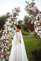 Beautiful fiancee in white wedding dress with bouquet stand  near the wedding arch of flowers....