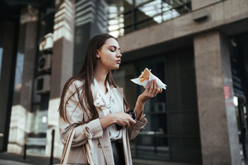 student goes to class and quickly bites a sandwich on the background of buildings