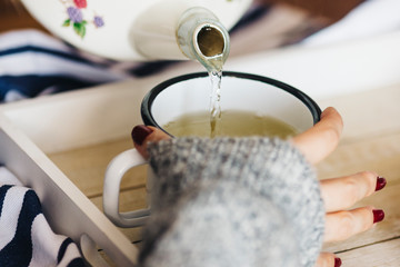 A female model is drinking herbal tea for flu, she is pouring herbal tea into a white enamel cup