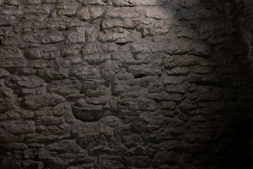 Fragment of a stone wall of a medieval city at night. The wall is lit by a lantern. The wall...