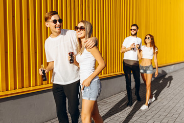 A group of young men and women, couples walking down the street with drinks in their hands