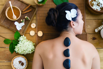 Top view young woman is getting hot massage, therapy. Basalt black stones are placed along spine of...