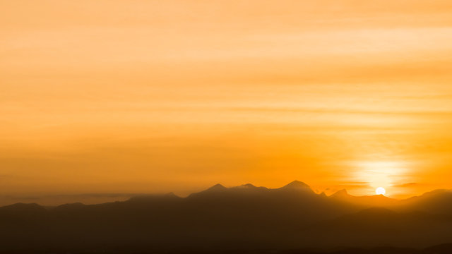 Anoitecer com sol se pondo atr&aacute;s das montanhas com c&eacute;u em tons de amarelo
