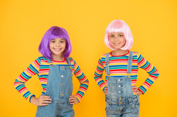 Life is better with friends. Happy girls friends on yellow background. Little friends smile in fashionable hair wigs and stylish overalls. Adorable small friends enjoy friendship. Playmates