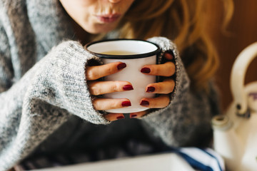A female model is drinking herbal tea for flu, she is pouring herbal tea into a white enamel cup