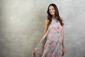 Portrait of an attractive young woman in a summer pink dress on a gray background