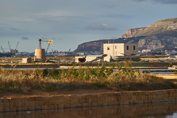 Fototapeta na wymiar Landscape picture of saltpans in traditional salt production close to sicilian city Trapani in italy, historical architecture like water lifting mill, old barrages and shallow ponds with sea water.