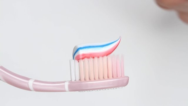 Putting toothpaste on a brush on white background