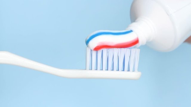Putting toothpaste on a brush on blue background