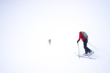 Two skiers struggling into a snow storm during a whiteout in the mountains