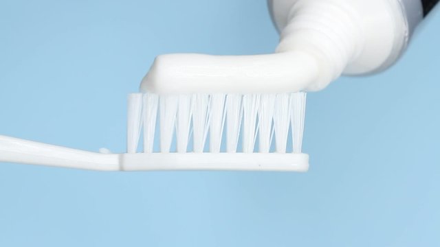 Putting toothpaste on a brush on blue background