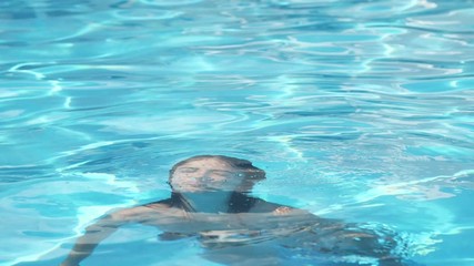 Stylish girl emerging on a water surface in azure swimming pond in slo-mo