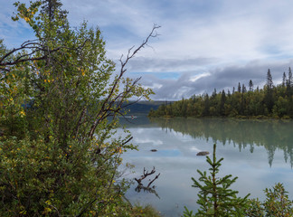 View over milky green Laitaure lake, hills, birch and spruce tree forest with small rowing boat. Lapland landscape at Kungsleden hiking trail. Blue sky white clouds.
