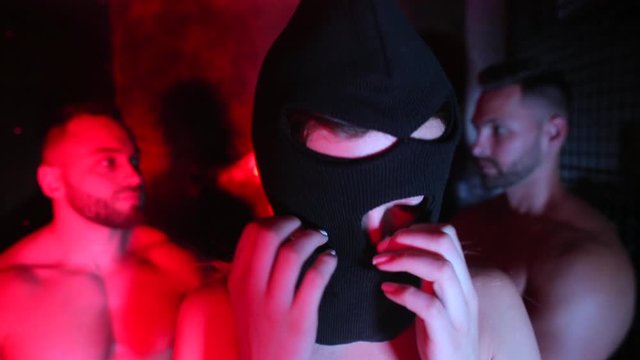 The girl puts on a balaclava. Against the background are men.